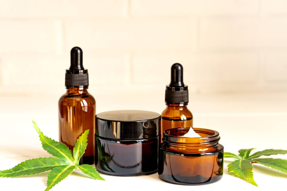 Cannabis face cream or serum or oil dropper concept. Natural cosmetic. CBD oil, THC tincture and hemp leaves on a wooden background. 