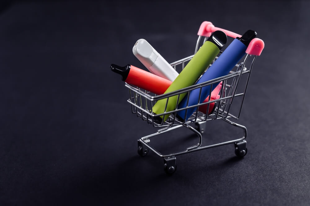 Disposable vapes in a shopping cart on a black background. Modern electronic cigarettes. 