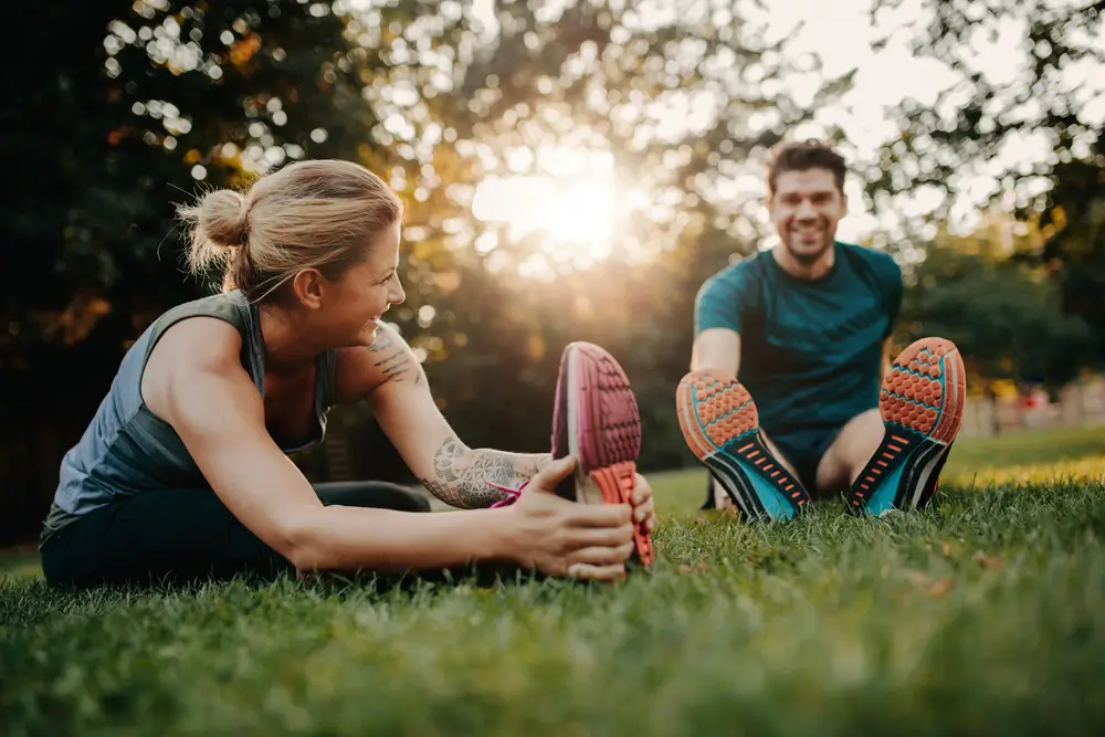 Fitness couple stretching outdoors in park. Young man and woman exercising together in morning. 