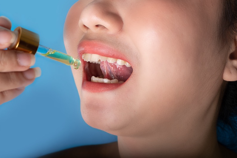 Beautiful asia young woman holding a dropper pipette sublingual Cannabis oil at blue background, Sick or unwell young women using a drop on his mouth for medicine, health and beauty concept