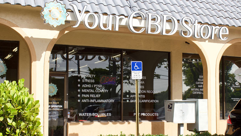 Your CBD Store, brick and mortar shop located in a strip mall with advertising in window, handicap parking space and sign in front .
