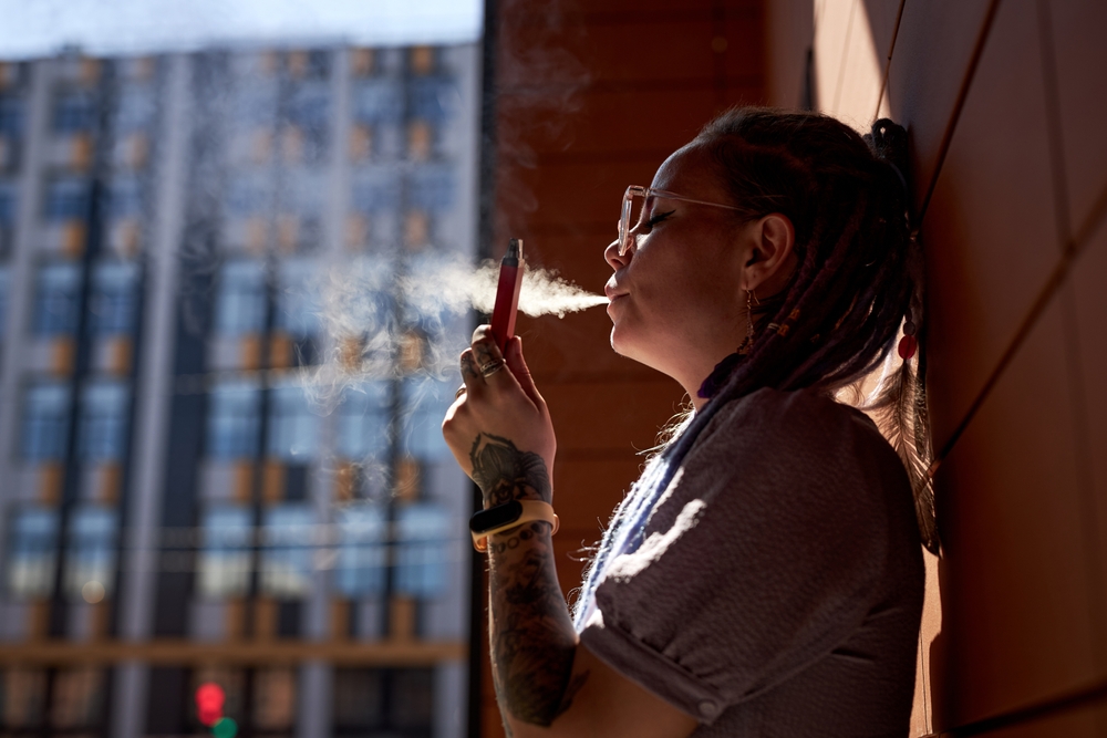 Young woman with vape pen in hand standing by wall of building
