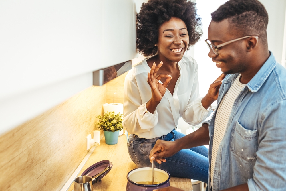 Happy black couple cooking and tasting healthy food in kitchen
