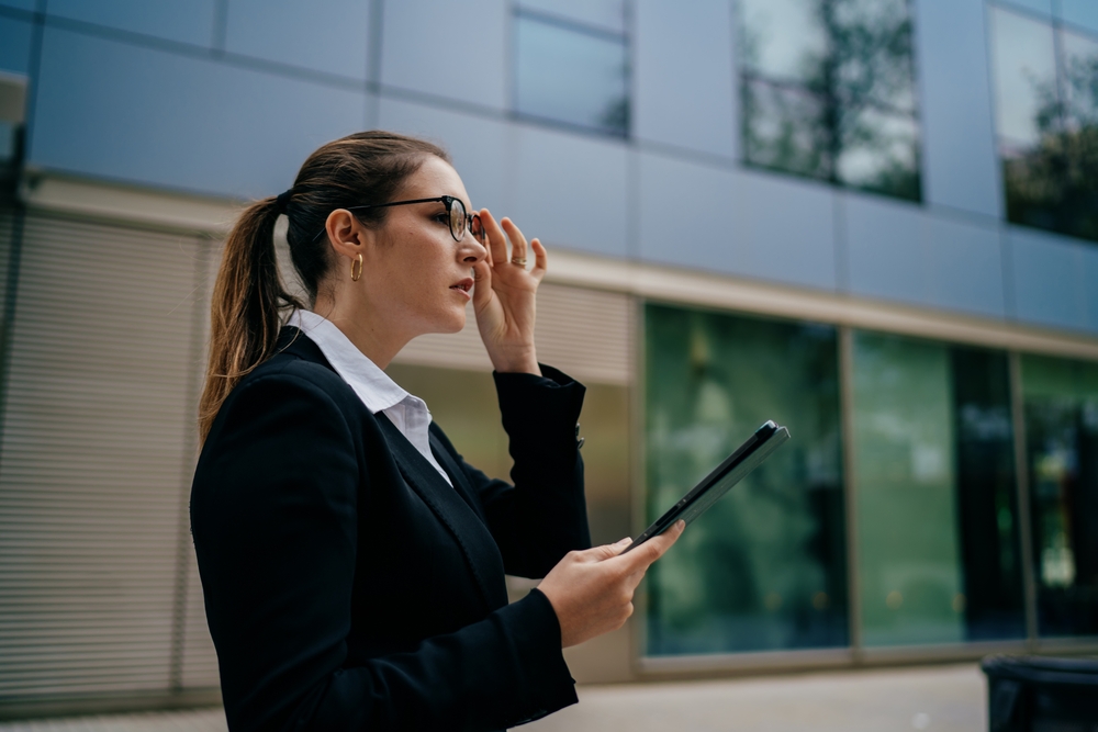 Side view of woman holding tablet and touching glasses, illustrating decisive attention