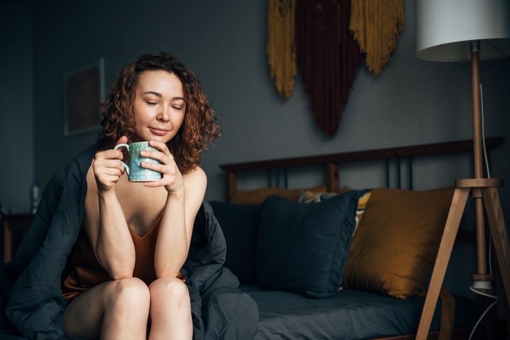 Girl drinking a relaxing drink with CBD tincture before going to bed, sitting in bed