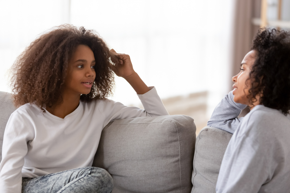 African adolescent girl sitting together with older sister friend or friendly nanny chatting sharing secrets